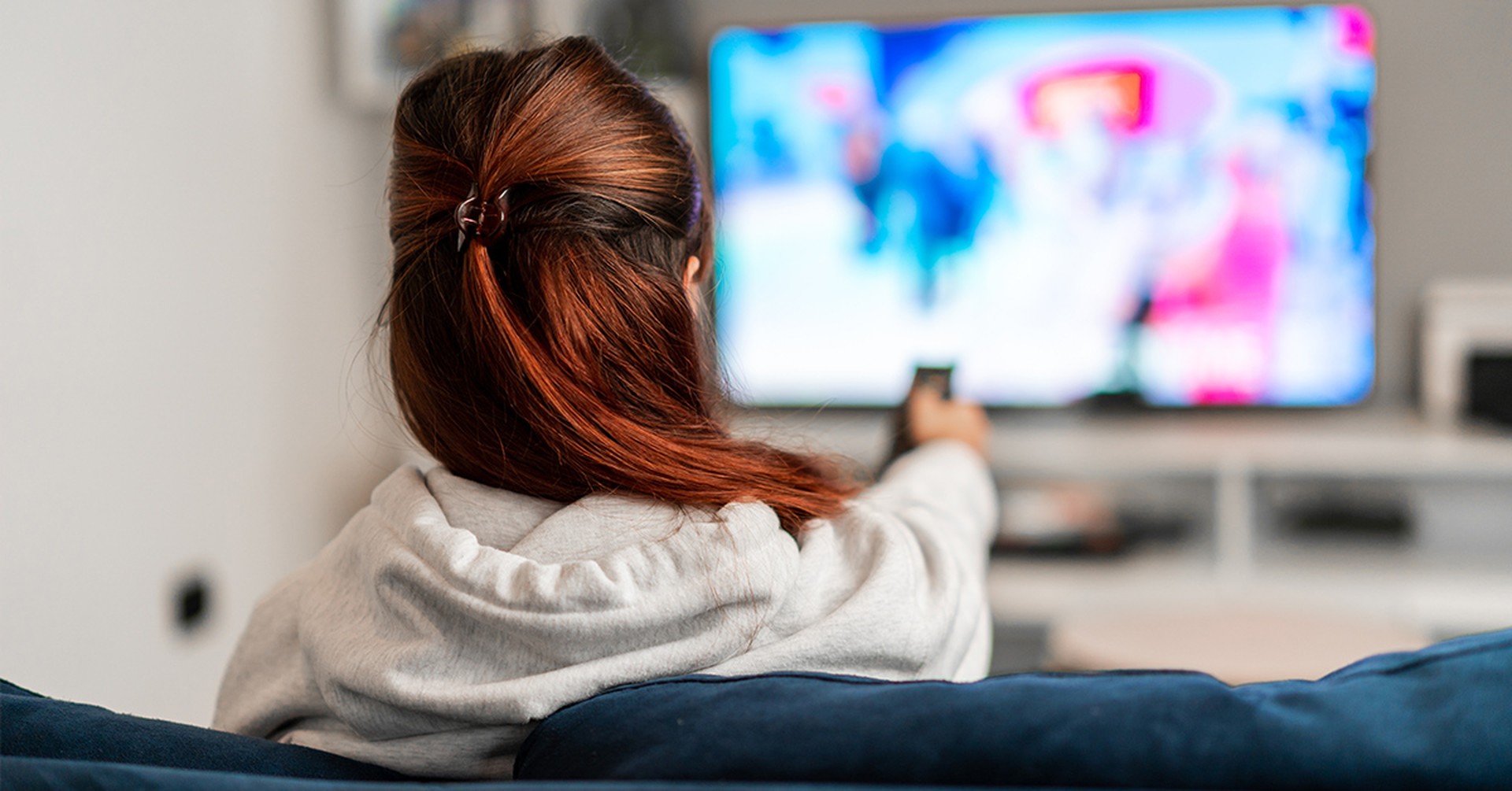 Frau sitzt vorm Fernseher mit Fernbedienung