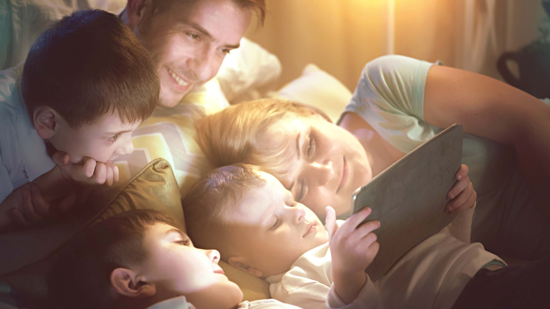 Familie liegt in Bett und schaut auf Tablet