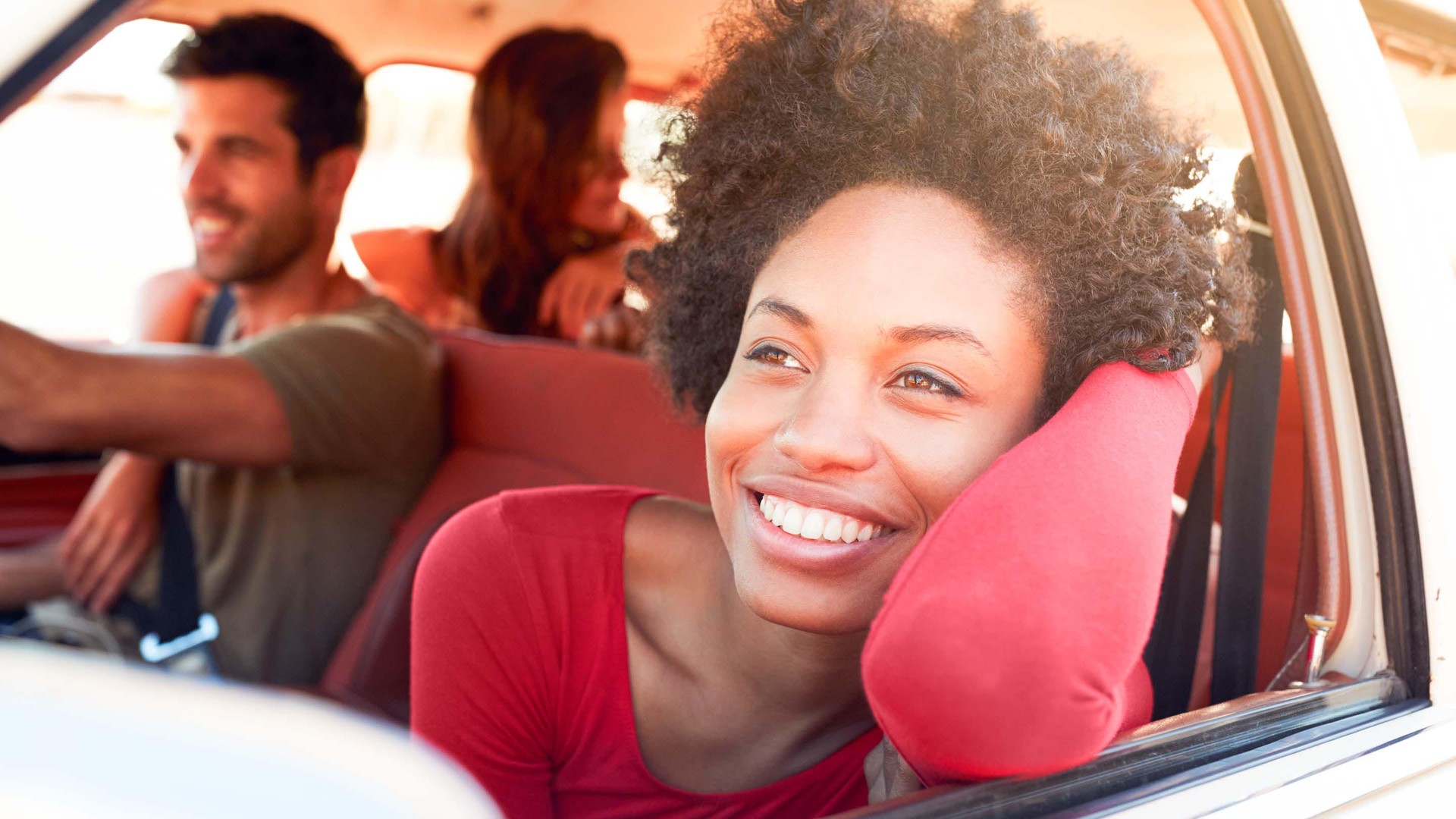 Freunde fahren in einem Auto, Frau schaut lächelnd aus dem Autofenster