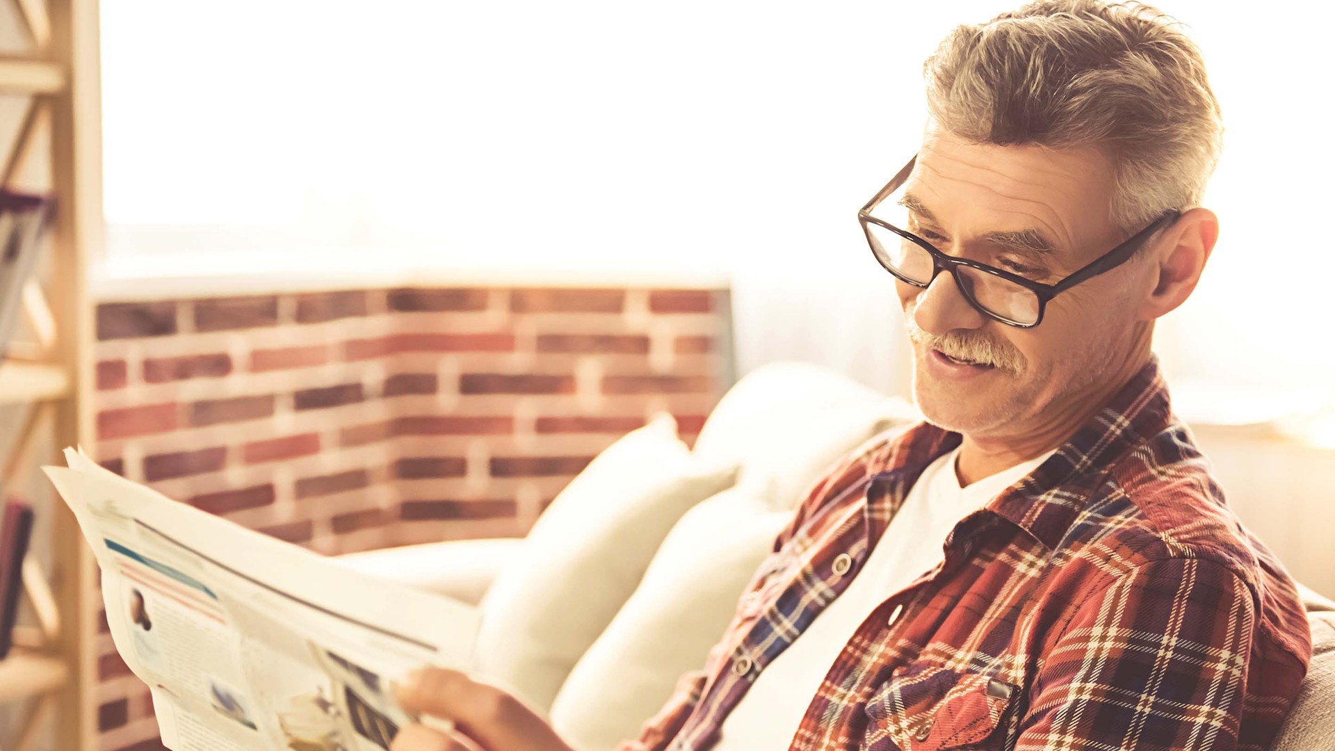 Älterer Mann sitzt auf Sofa und liest Zeitung